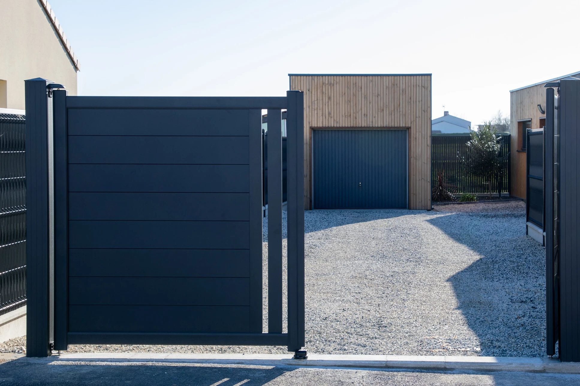 Entrée résidentielle moderne avec portail coulissant anthracite ouvert sur allée gravillonnée menant à garage contemporain