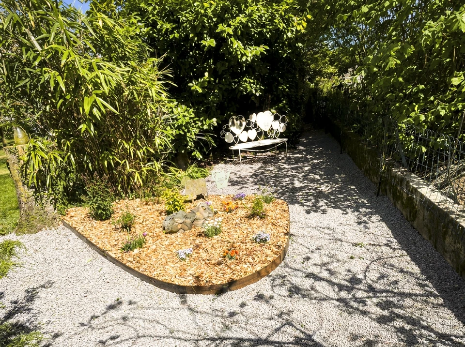 Paysage extérieur d'une maison montrant à la fois des éléments d'aménagement paysager et de maçonnerie : au premier plan une terrasse pavée ou dallée récemment construite, flanquée de massifs de plantes bien entretenus, d'arbustes taillés et de pelouse verte. L'arrière-plan peut inclure une clôture en aluminium ou un portail. La scène doit montrer clairement les deux domaines de compétence : espaces verts d'un côté et structures maçonnées de l'autre, illustrant ainsi le double savoir-faire de l'entreprise.