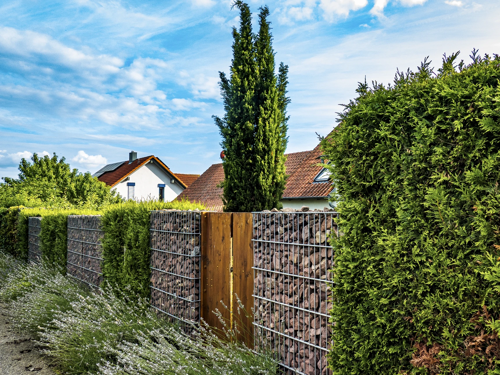 Une clôture en aluminium moderne installée le long d'une propriété résidentielle, photographiée en extérieur en lumière naturelle. La clôture doit être complètement posée et fonctionnelle, encadrant élégamment un espace extérieur aménagé (jardin, terrasse ou cour). L'image doit montrer clarirement la clôture en position d'utilisation finale, mettant en valeur à la fois son aspect sécurisé et son attrait esthétique pour la propriété.