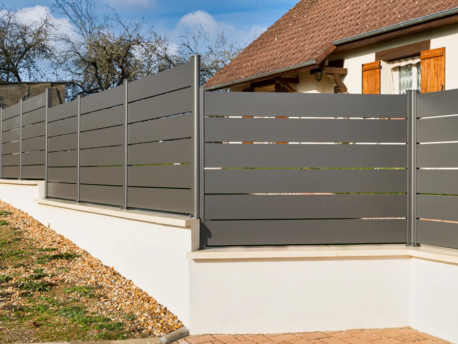 Scène extérieure résidentielle montrant une clôture moderne installée le long d'une allée pavée claire