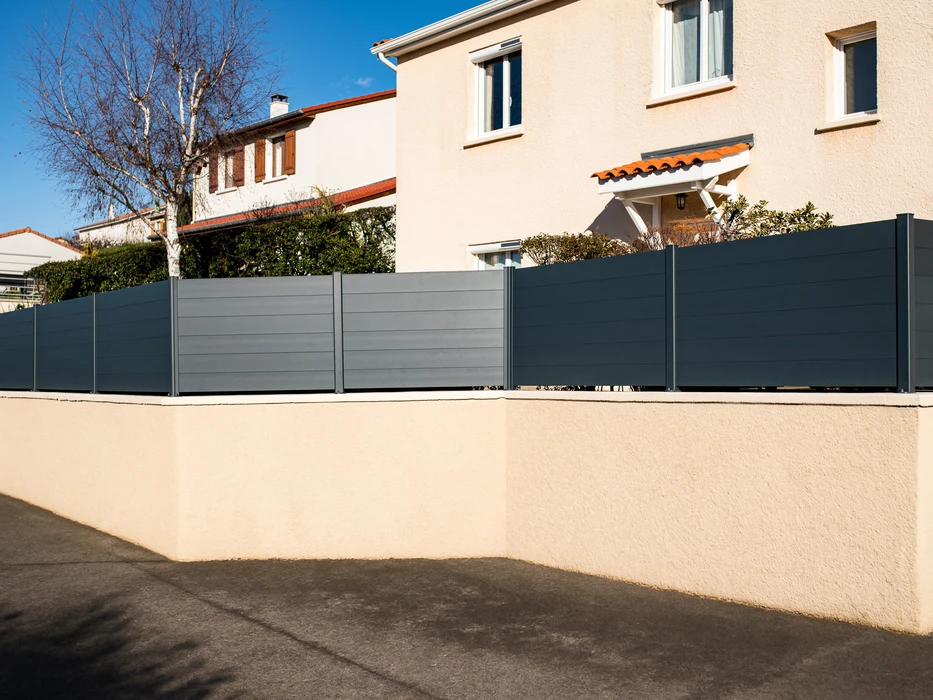 Scène extérieure résidentielle montrant une clôture moderne installée le long d'une allée pavée claire
