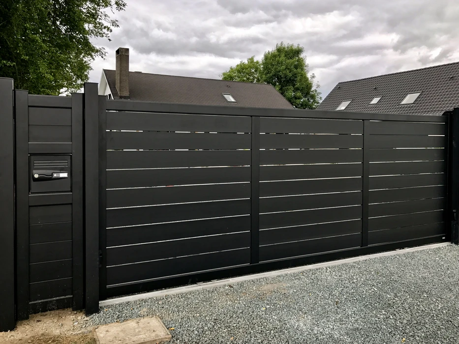 Scène extérieure résidentielle montrant une clôture moderne installée le long d'une allée pavée claire