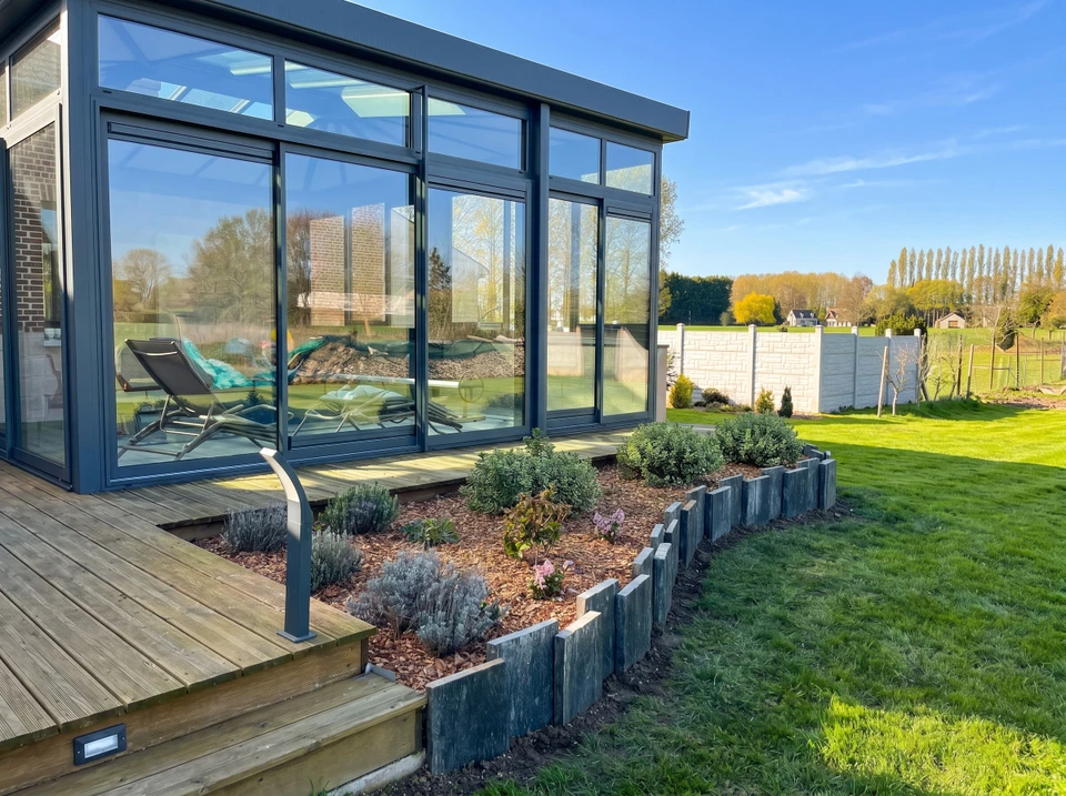 Aménagement paysager extérieur avec arbre fleuri rose central entouré de massifs arbustifs, conifères et fleurs blanches sur pelouse verte