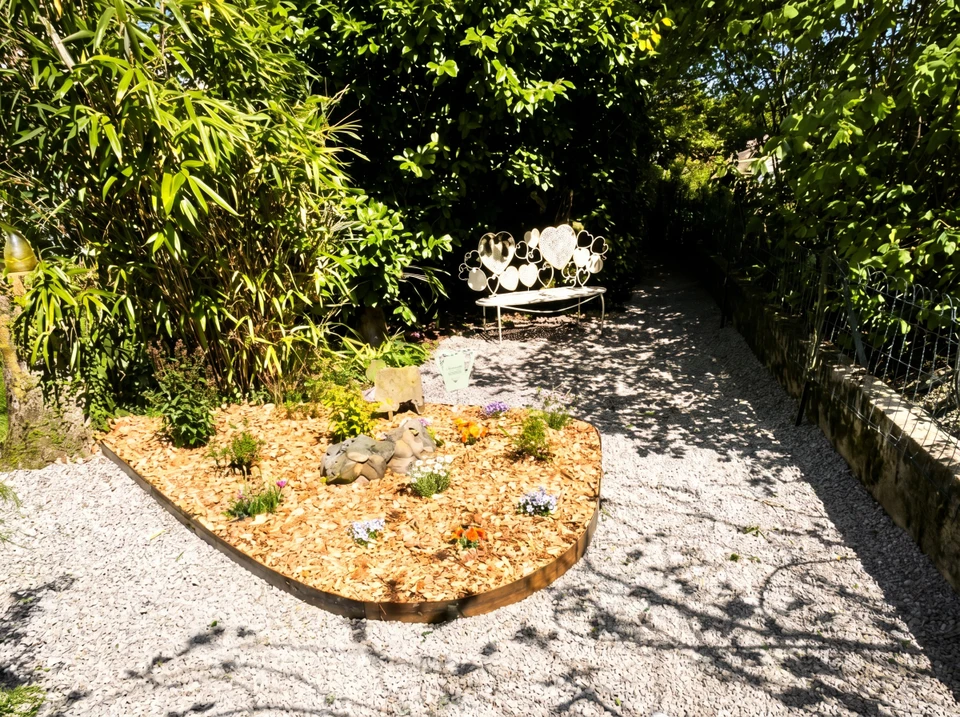 Paysage extérieur d'une maison montrant à la fois des éléments d'aménagement paysager et de maçonnerie : au premier plan une terrasse pavée ou dallée récemment construite, flanquée de massifs de plantes bien entretenus, d'arbustes taillés et de pelouse verte. L'arrière-plan peut inclure une clôture en aluminium ou un portail. La scène doit montrer clairement les deux domaines de compétence : espaces verts d'un côté et structures maçonnées de l'autre, illustrant ainsi le double savoir-faire de l'entreprise.